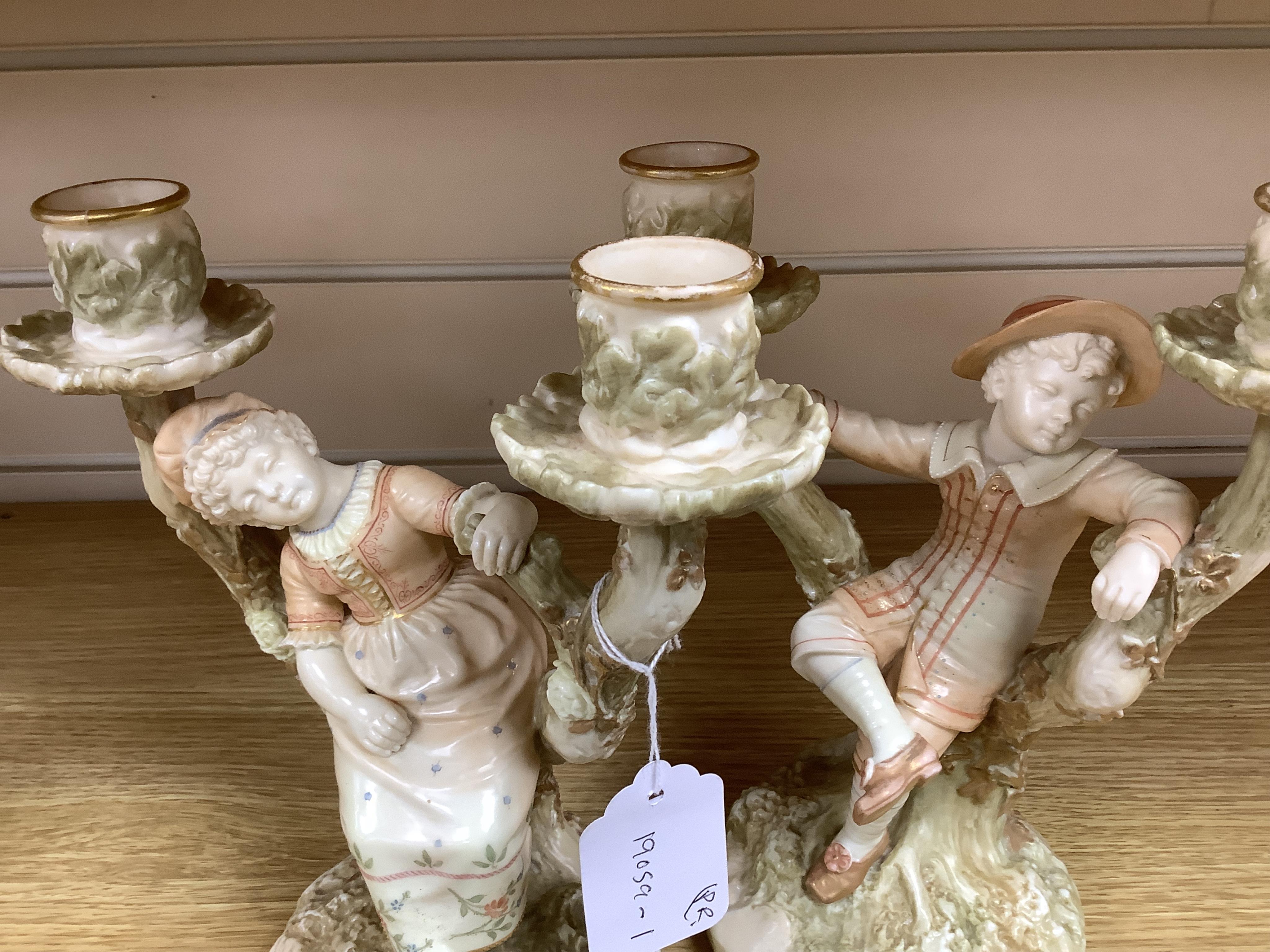A pair of late 19th century Royal Worcester Kate Greenaway style figural two branch candelabra, modelled by James Hadley 22.5cm high